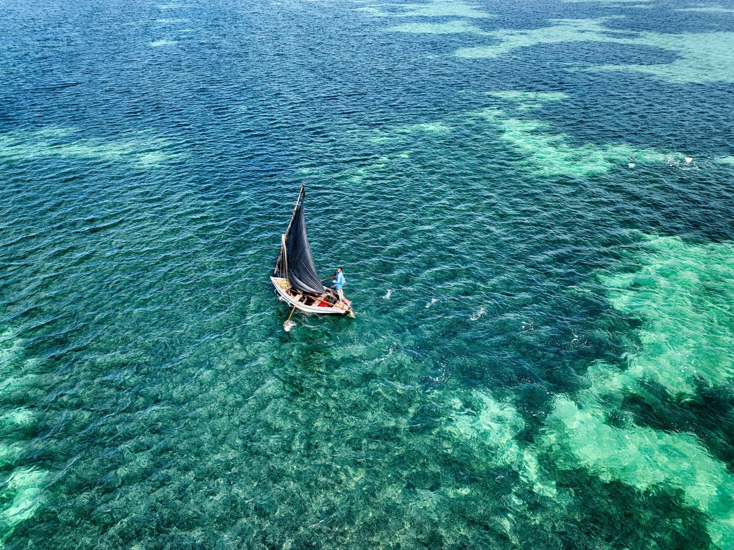 A traditional dhow under sail over turquoise water, seen from above