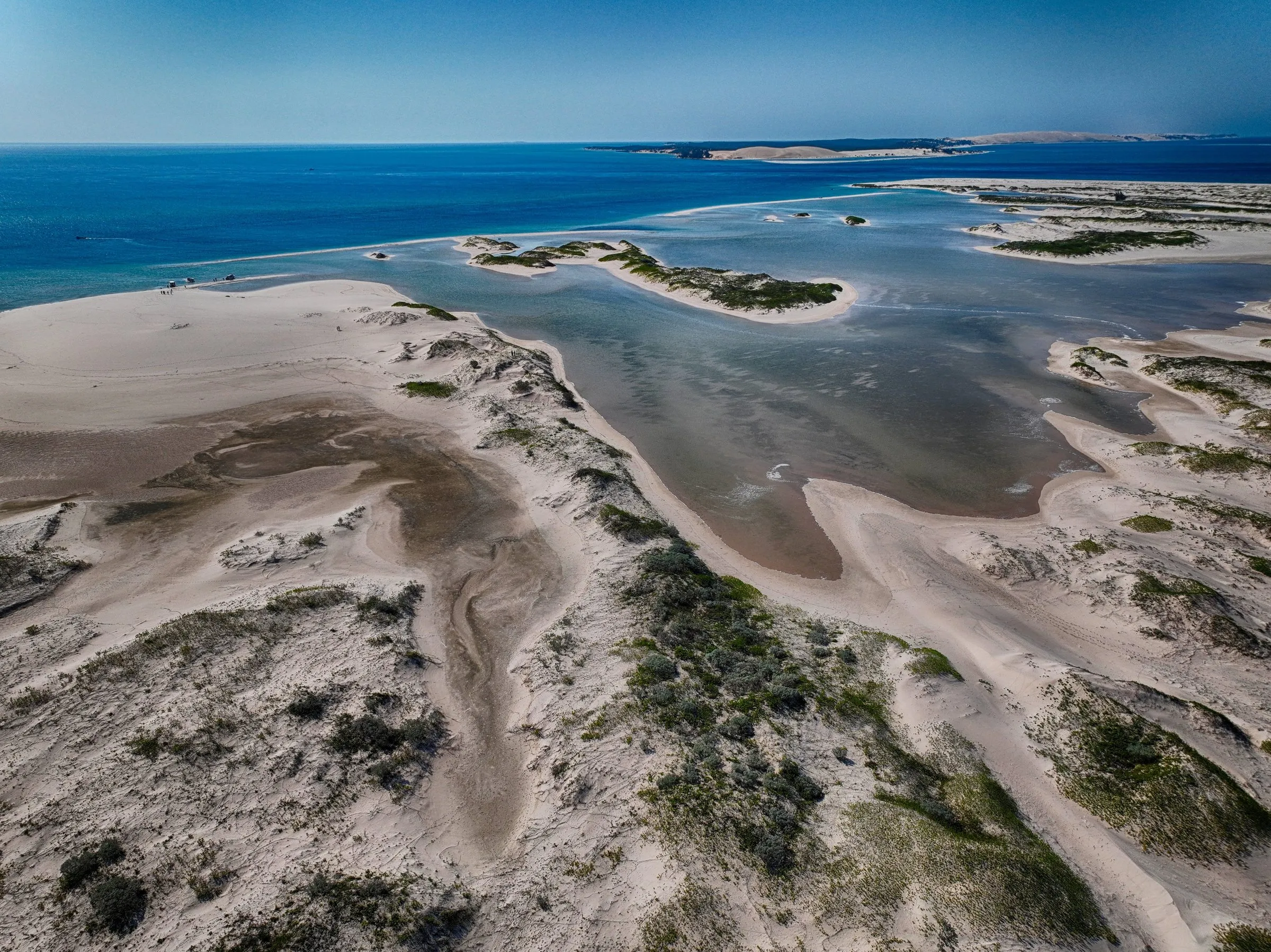 Sweeping white sandbanks and a tidal channel meeting the open ocean